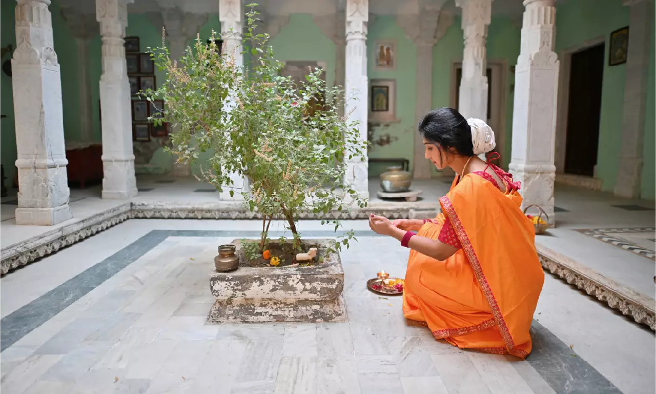 Woman in traditional orange saree performing Tulsi puja with diya on Kartik Poornima